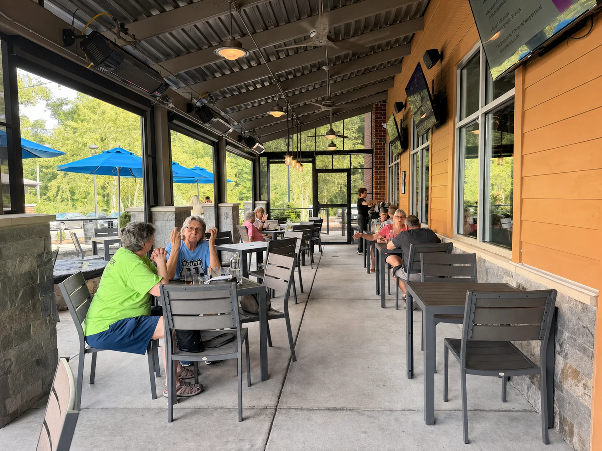 Guests at tables down the length of the patio, blue umbrellas open past the edge