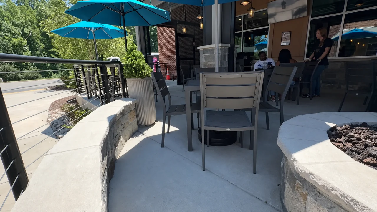 A stone fire pit filled with lava rock at the end of the patio, chairs pulled up beside it