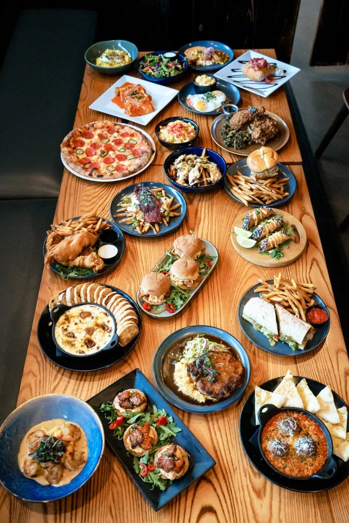 A full table spread of pizzas, burgers, shareables, and wood-fired mains