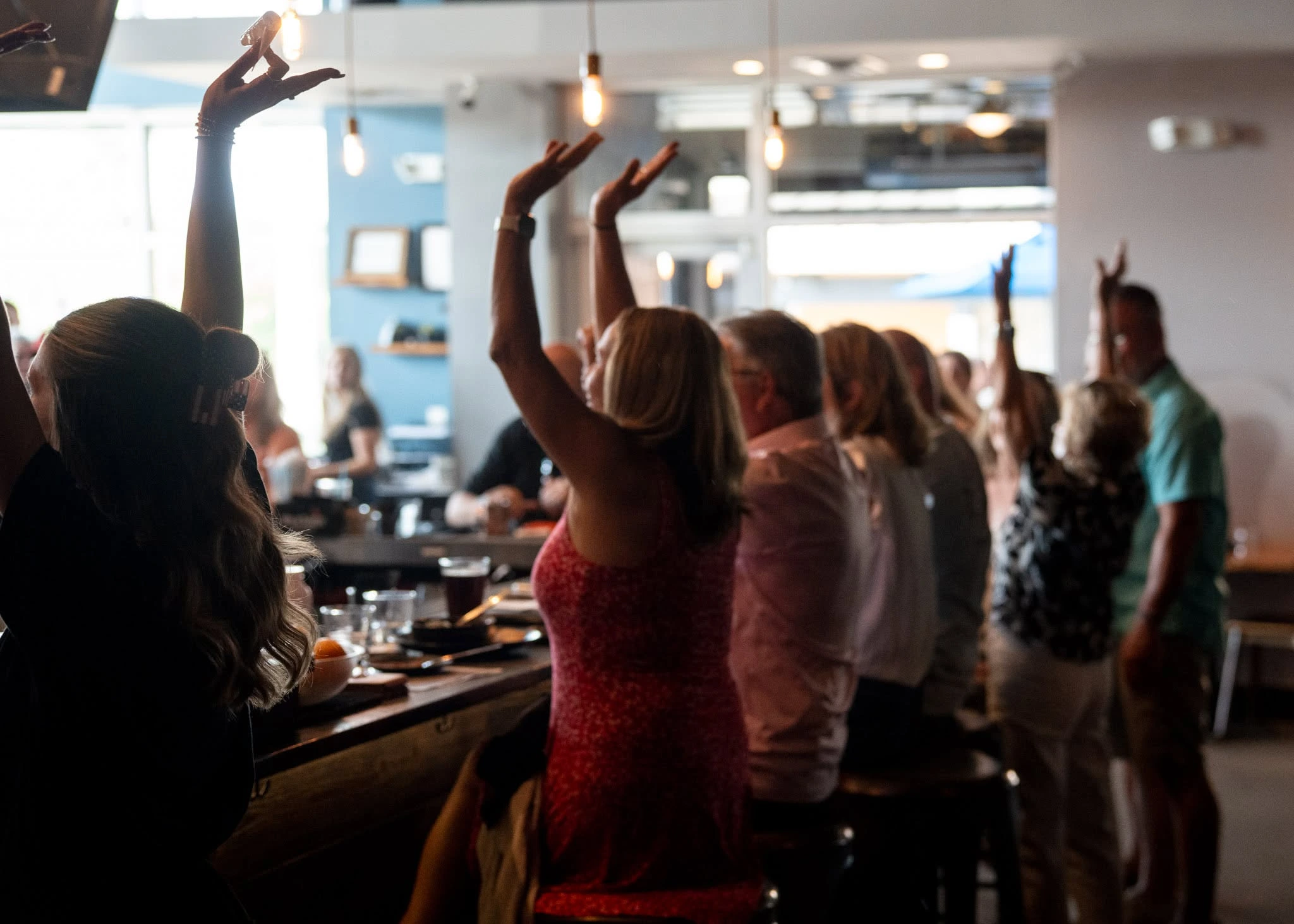 Guests raising their hands together during a community celebration in the dining room
