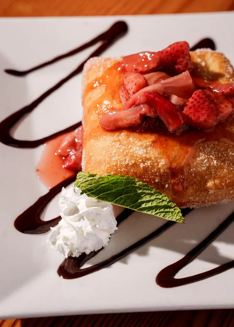 Warm strawberry beignet with whipped cream and chocolate drizzle